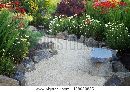 A curved garden path edged with stones winds through a perennial garden with crocosmia and dasies.
