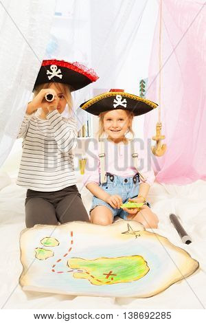 Two cute girls in costumes of pirates looking through a toy spyglass