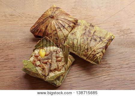 Sticky rice wrapped in lotus leaf or Zongzi is traditional Chinese food on wooden background.