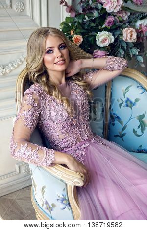 young sexy blonde girl sitting on the couch in Lacy pink dress turns her head and smiles portrait