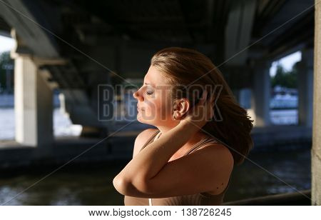 Portrait of woman smiling outdoors near the stone bridge. She touches her hair in the wind.