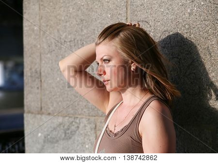 Portrait of woman smiling outdoors near the stone bridge. She touches her hair in the wind.