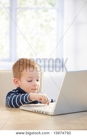 Raního batole přes notebook doma, sedí u stolu.?