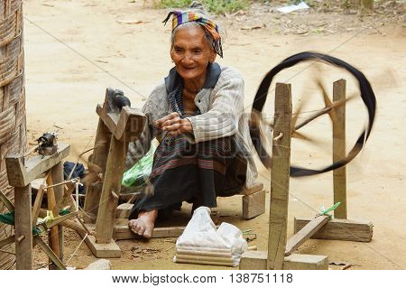 MUANG NGOI, LAOS - FEBRUARY 15, 2016: Old woman spinning on traditional spinning wheel in a minority village on February 15, 2016 in Laos, Asia