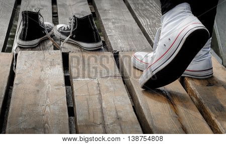 Teenager wearing white shoes standing behind black snickers on the wooden bridge, choice concept