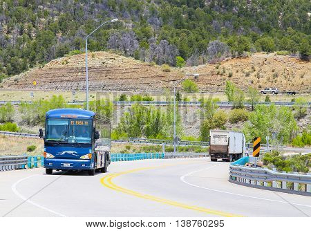 RATON, NEW MEXICO, USA - MAY 20, 2015: Greyhound Bus going to El Paso driving up an ascending road in the back a truck is driving down.