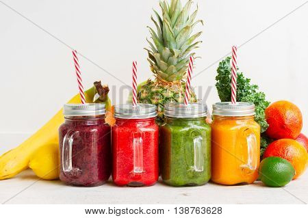 Colorful smoothy drinks in glass jars with straws and igredients