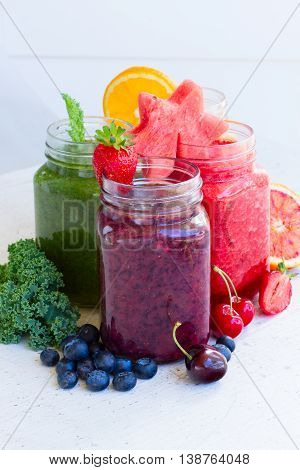 Colorful fresh berry and fruits smoothy drinks in glass jars with igredients on white table close up