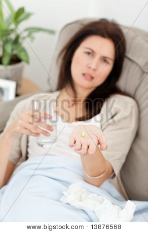 病気の女性が自宅のソファに彼女の薬の服用