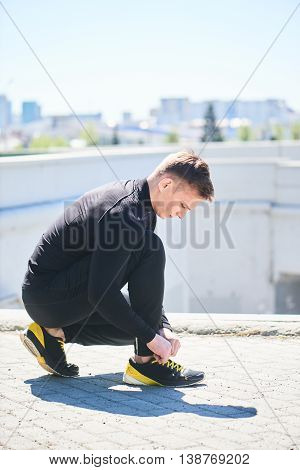 The athlete straightens his sneakers against the background of the city