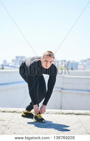 The athlete straightens his sneakers against the background of the city