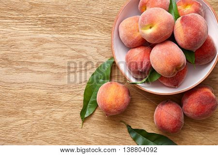 Ripe peaches with leaves in a terracota bowl on a wooden background