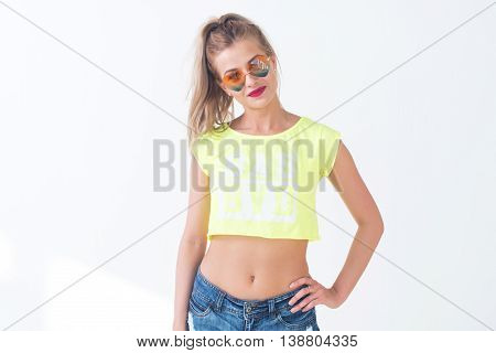Young woman posing, alone wearing bright yellow t-shirt, denim shorts with naked, stomach. Female model presenting casual, summer look on white background