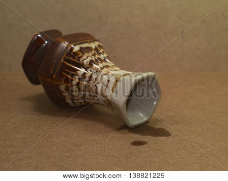 Beautiful vintage brown ceramic vase falling on wooden board with a spill of water