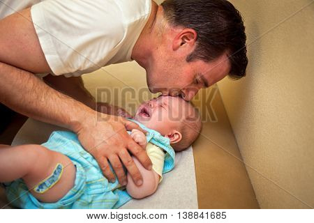 A father tries to comfort his 2 month old son with a kiss after the boy received his vaccination shots.