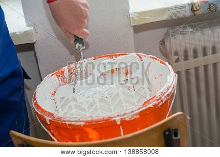 Painter and interior decorator touches paint roller to paint grid from