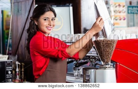 Barista in Indian cafe filling coffee grinder with coffee beans