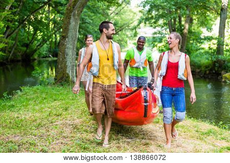 Friends carrying kayak or canoe to forest river