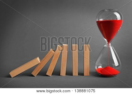 Hour glass blocked row of falling dominoes on grey background