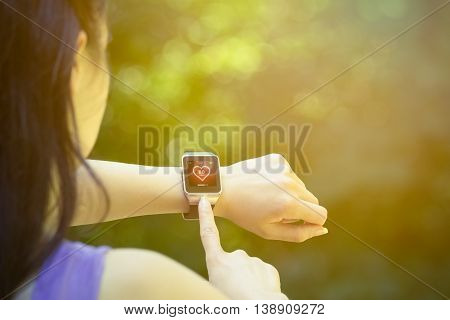 Young female athlete looking at heart rate app and checking beats per minute on her smart watch in the park. Fitness, healthy lifestyle and new technology concepts.