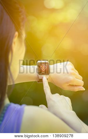 Young female athlete looking at heart rate app and checking beats per minute on her smart watch in the park. Fitness, healthy lifestyle and new technology concepts.