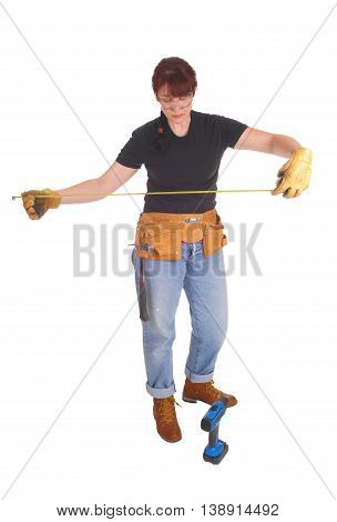 A tall middle age woman in jeans and a tool belt and drill measuring for her job standing isolate for white background.