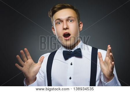Closeup Portrait of handsome boy with astonished expression while standing against grey background.