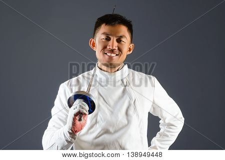 Fencing athlete posing with a sword or epee on gray background.