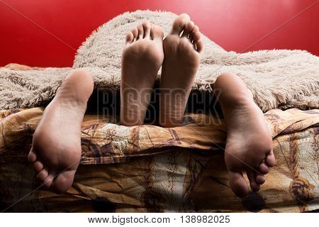 Two pairs of male and female feet seen from under the blanket. sleep together, lovers having sex.