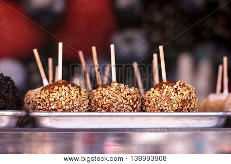 Candy caramel apples on sticks with nuts on a counter at a county fair ground in summer.
