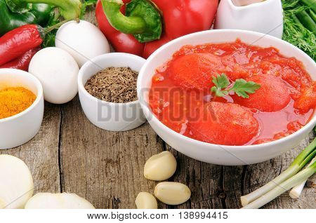 Different ingredients for cooking healthy and tasty food. Tomatoes in own juice spicy seasoning pepper onion garlic olive oil and eggs on a wooden table with copy space