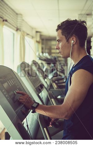 Handsome Athlete In Earphones Setting Program On Threadmill