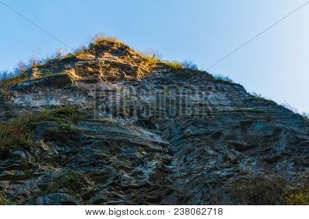 Low-angle View Of A High Steep Rocky Mountain With Cliff Illuminated By The Sun
