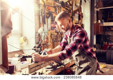 profession, carpentry, woodwork and people concept - carpenter working with plane and wood plank at workshop