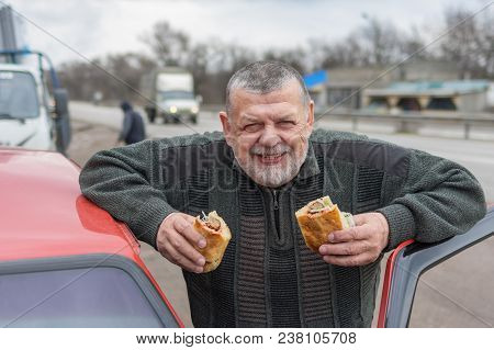 Portrait Of Caucasian Senior Driver Eating Lyulya Kebab In Lavash Near His Car