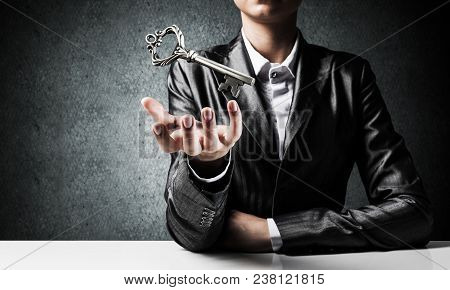 Cropped Image Of Businessman In Suit Keeping Big Key In Hand With Dark Wall On Background.