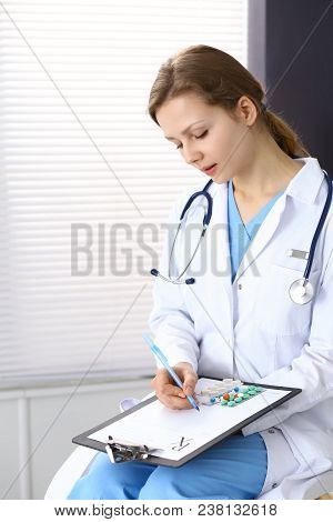 Woman Doctor Write Prescription While Sitting In Hospital Office. A Lot Of Various Colored Pills Liy