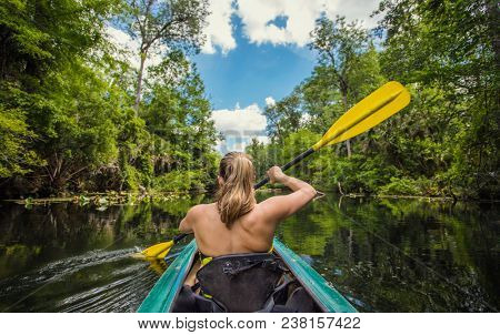 Adventuresome Woman kayaking along a beautiful tropical jungle river. Paddling along a calm beautiful river in a scenic natural backdrop
