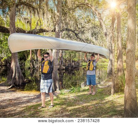 Two Adventuresome men ready go canoeing on a tropical river as they carry their canoe into the water smiling and ready for fun time in the outdoors
