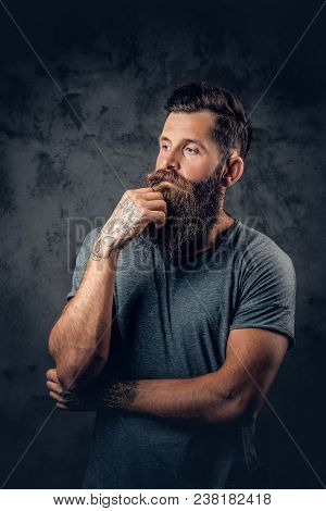 Brutal Bearded Male With Tattooed Arms Over Dark Grey Background.