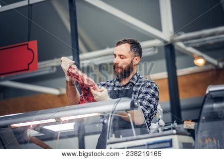 Bearded Meat Seller Dressed In A Fleece Shirt Serving Fresh Cut Meat In A Market.