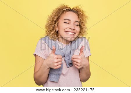 Girl Is Smiling And Showing Big Thimbs Up. She Is Happy. Isolated On Yellow Background