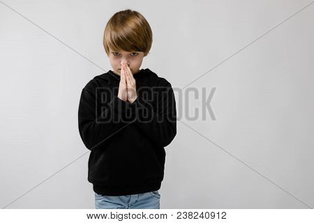 Portrait Of Cute Little Boy Wearing Black Hoody And Holding Hands Clasped In Pray Or Pleading Or Apo