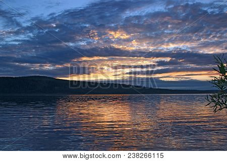 Dark Blue Sky With Golden Patches Gloomy Hangs Over River Water And Its Reflection