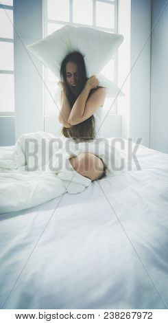 Young caucasian woman covering her head and ears with pillows