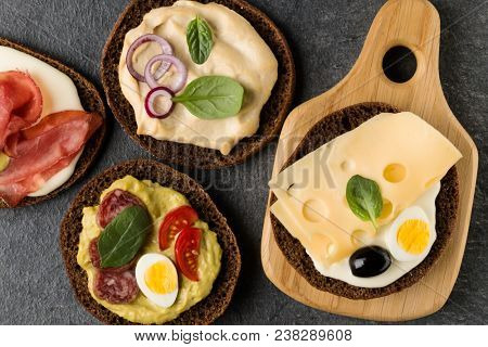 Open  faced  sandwich canape or crostini on a wooden serving board on dark stone background closeup. Top view.