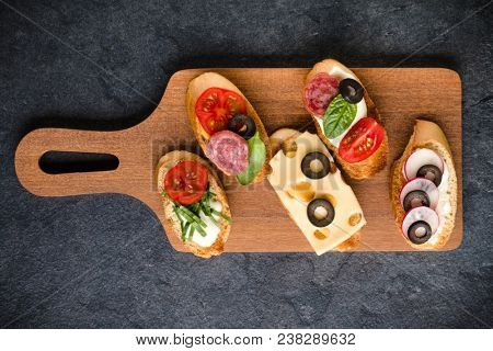 Open faced sandwich canape or crostini on a wooden serving board on dark stone  background closeup. Top view.