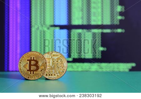 Two Gold Bitcoins Lie On The Green Surface On The Background Of The Display, Which Shows The Process