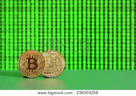 Two Gold Bitcoins Lie On The Green Surface On The Background Of The Display, Which Shows The Process