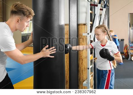 Little girl with trainer near punchbag in gym
